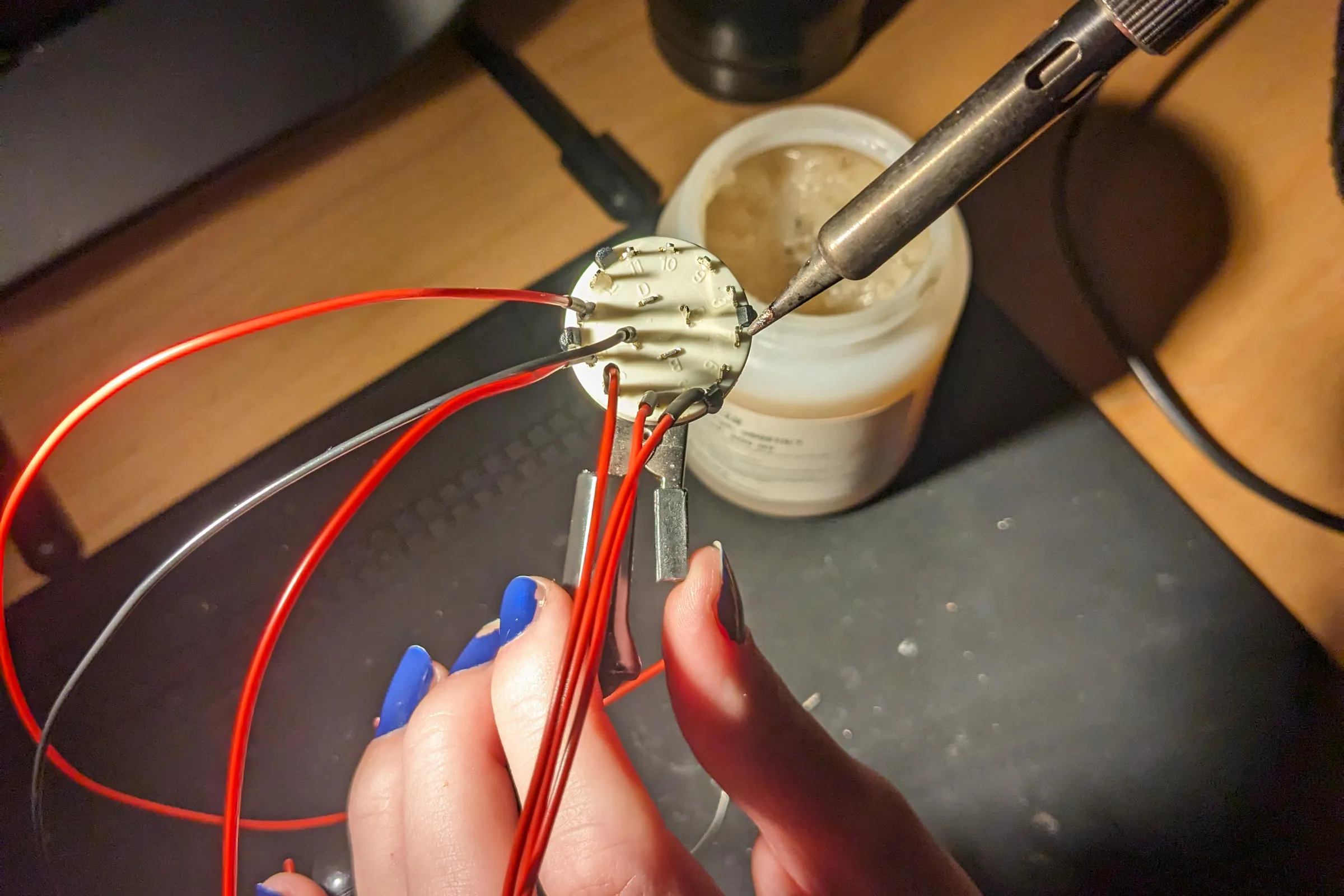 Hands soldering wires to a rotary potentiometer component for physical dial inputs.